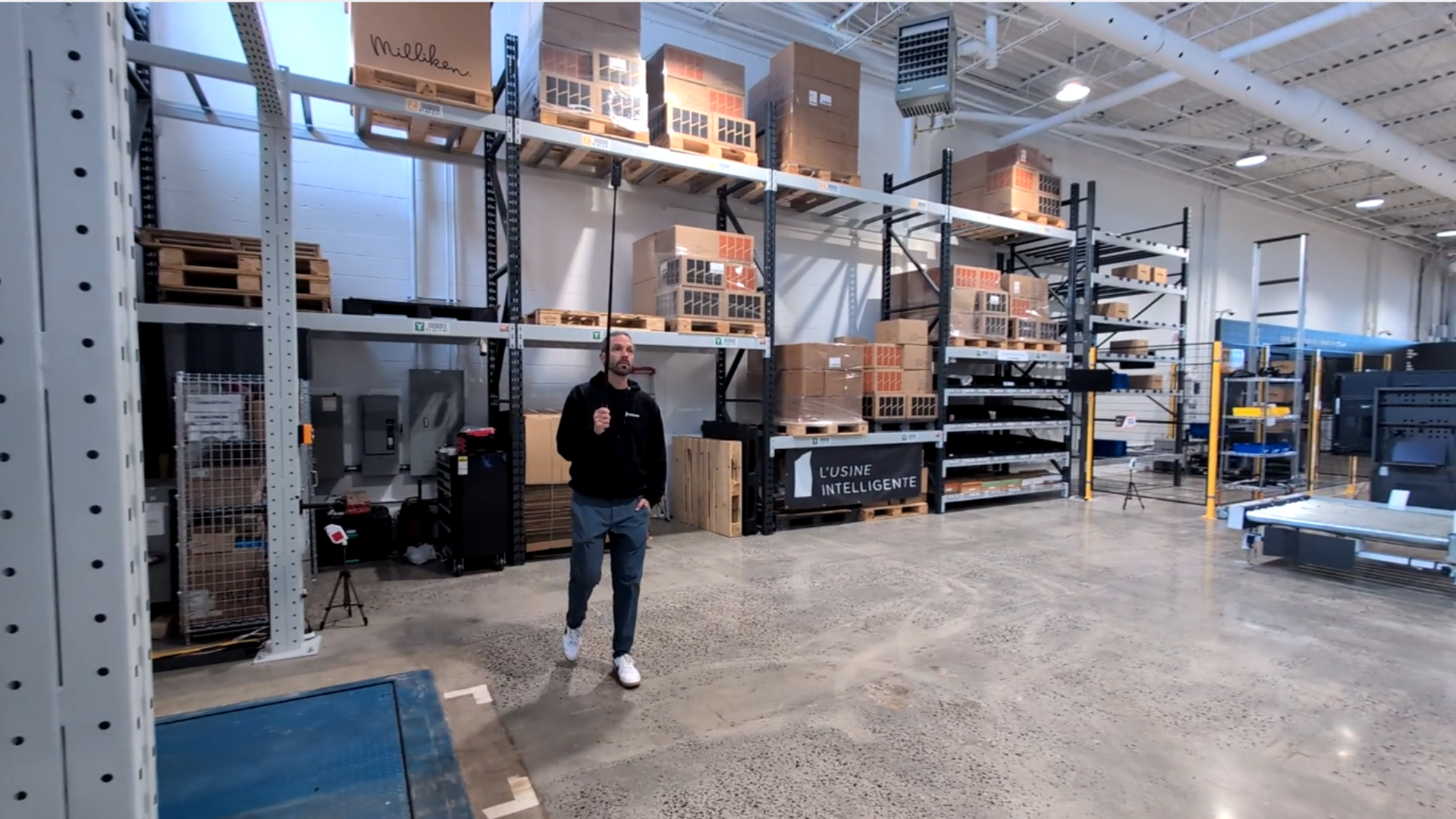 A technician conducting a digital site survey on a factory floor, using an Insta360 X5 camera and an extended selfie stick to capture comprehensive reality data